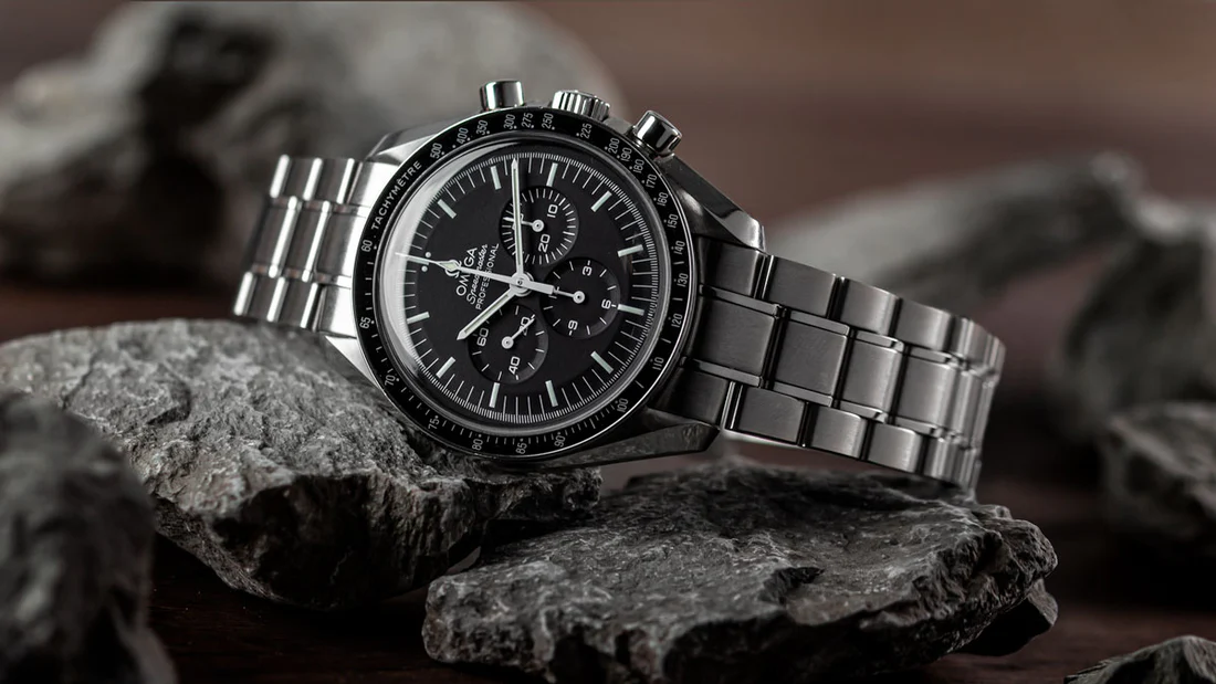 Omega Speedmaster Professional Moonwatch sur bracelet acier, posée sur des roches